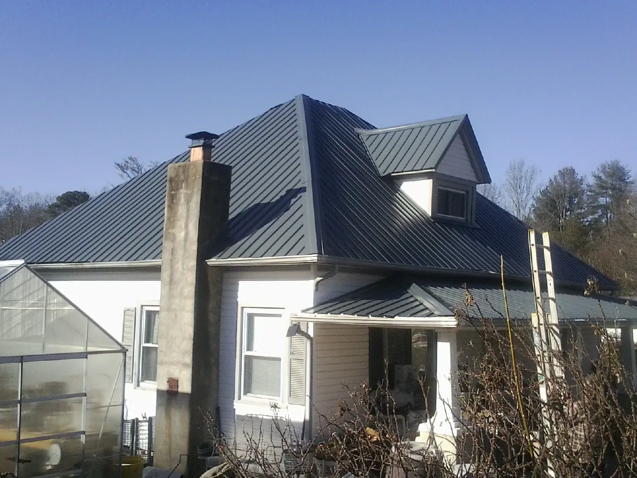 Dark blue standing seam metal roof on a white farmhouse with dormer — Slate & Tile Roof Repair by Roofing Brothers in Bomont
