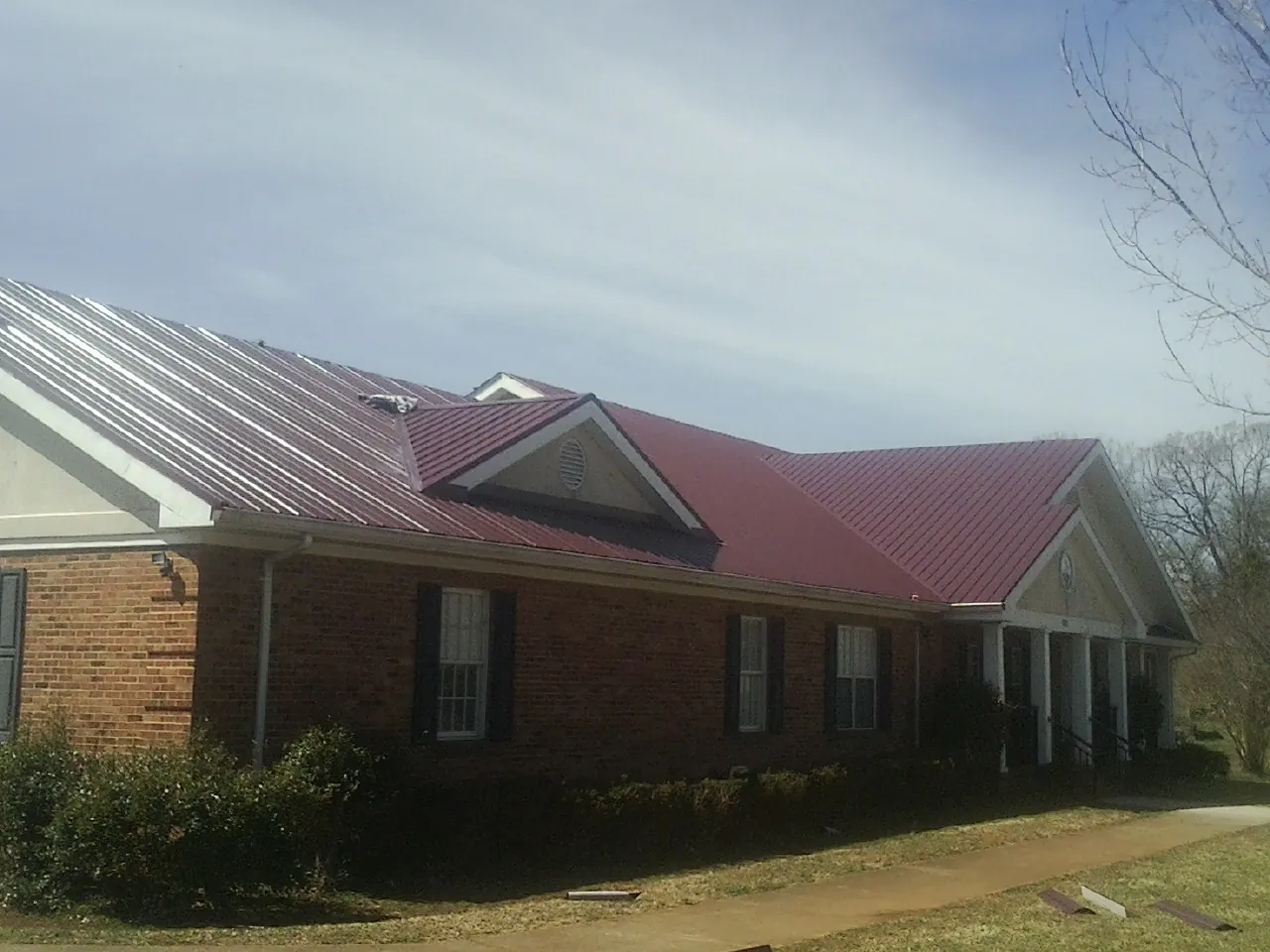 Red metal roof with gabled entries on a long brick building, from a Hail Damage Roof Repair job in Bomont
