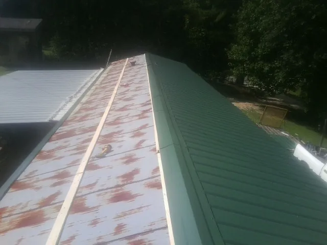 Old rusted panels beside newly installed green metal roofing — Wind Damage Roof Repair by Roofing Brothers in Bomont