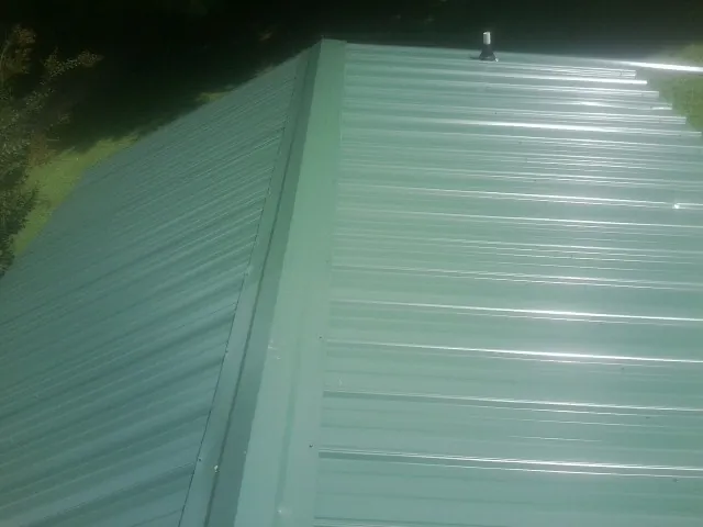 New green metal panels meeting at the ridge of a roof — Flat Roof Repair work by our crew in Bomont