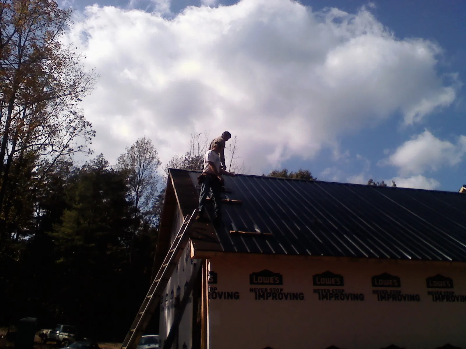 Roofer fastening dark metal panels high against a cloudy sky, from a Roof Inspection job in Bomont