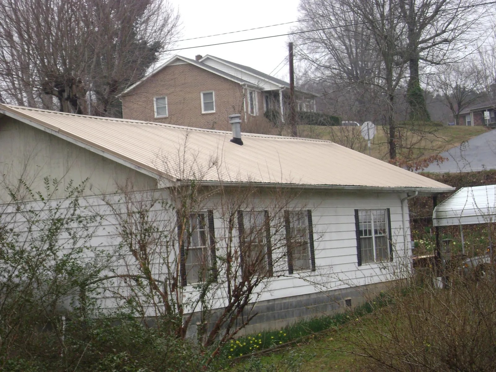 Tan metal roof on a white sided house set into a hillside — Commercial Roofing by Roofing Brothers in Bomont