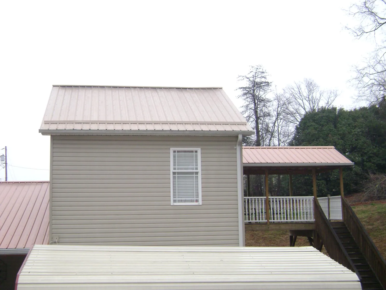 Tan metal roofs on a two story addition and attached porch, from a Roof Replacement job in Bomont